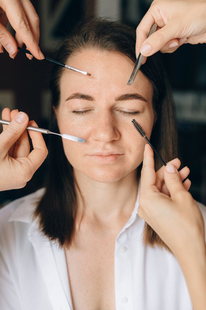 Close-up of a woman with eyes closed receiving makeup using various brushes and tools.
